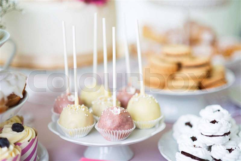 Table with white and pink cake pops on cakestand, meringues and cupcakes. Candy bar, stock photo