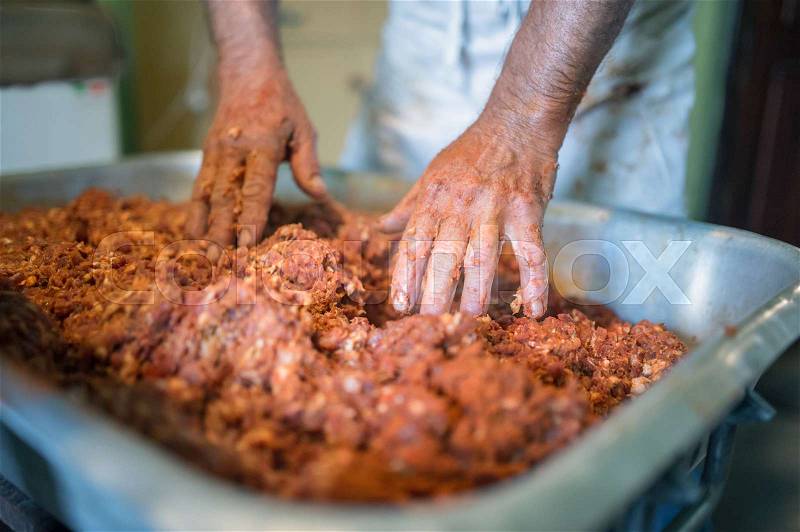 Unrecognizable man making sausages the traditional way at home. Mixing meat and spices in the bowl, stock photo