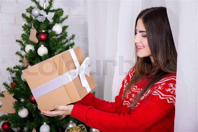 Surprised young beautiful woman with gift box and Christmas tree, stock photo