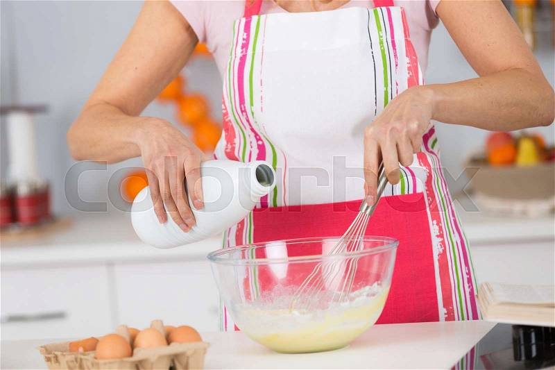 Pouring milk into a pot to prepare cake, stock photo