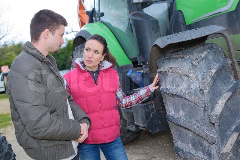 Attractive woman selling brand new tractor to beginner farmer, stock photo