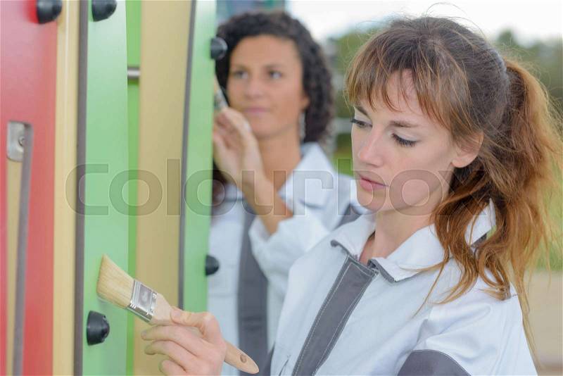Women painting outdoor play equipment, stock photo