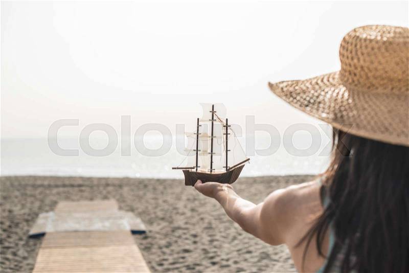 Woman with hat hold boat model on the beach, stock photo