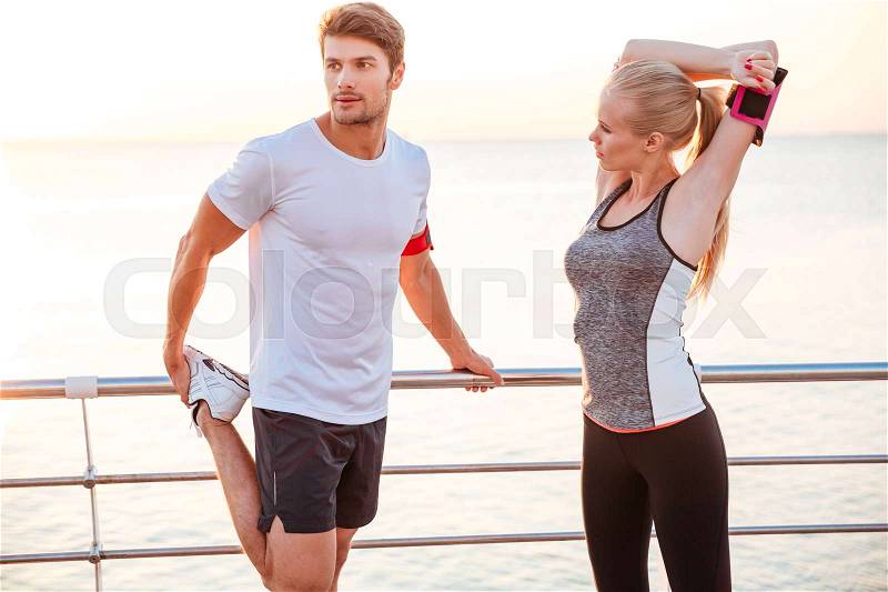 Athletic young couple stretching out after running at the beach pier, stock photo