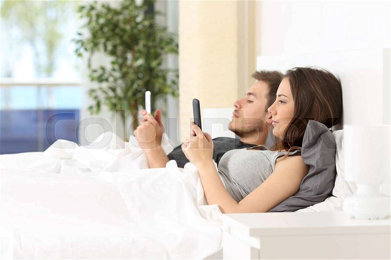 Angry couple everyone with their own phones lying on the bed at home, stock photo
