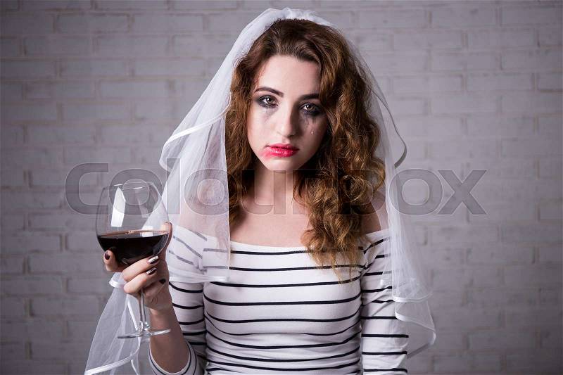 Portrait of sad bride crying and drinking red wine, stock photo