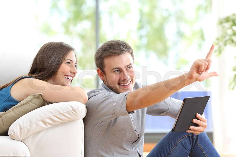 Happy couple sitting and planning new decoration with a tablet on line at home with a window in the background, stock photo
