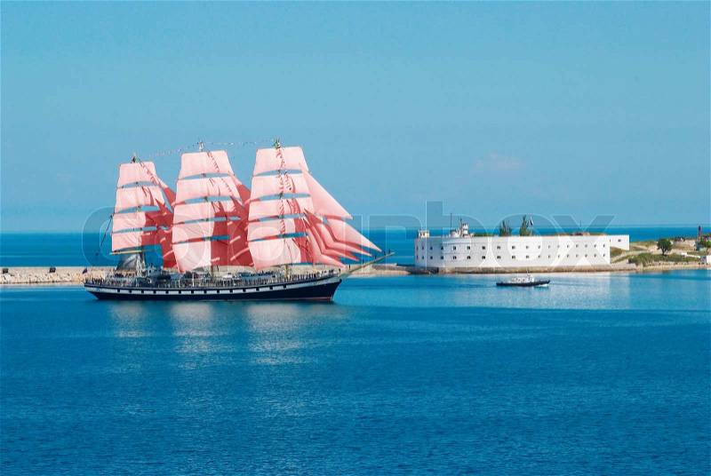 Sailing ship with red sails entering to the bay, stock photo