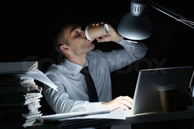 Manager working in office at night and drinking coffee at his workplace , stock photo