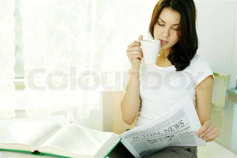 Young girl reading newspaper and drinking tea, stock photo