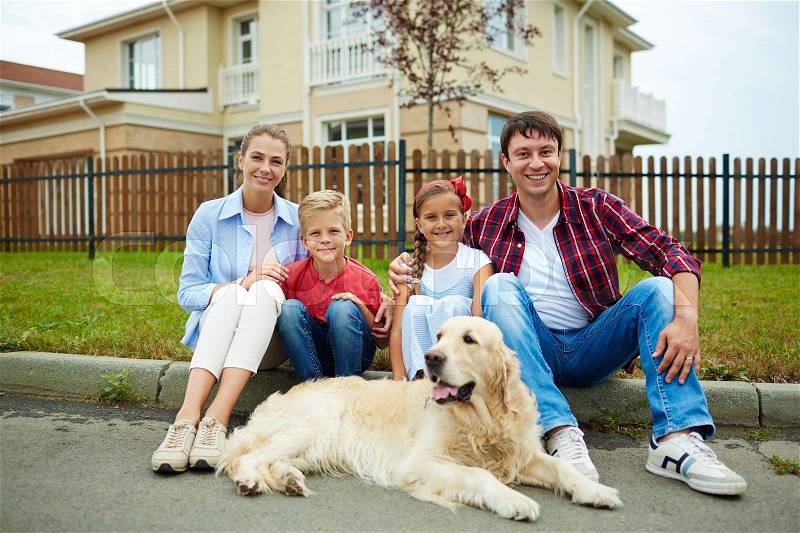 Family of four and their pet sitting by their new house, stock photo