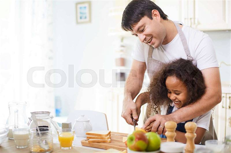 Young father showing his daughter how to cut bread, stock photo