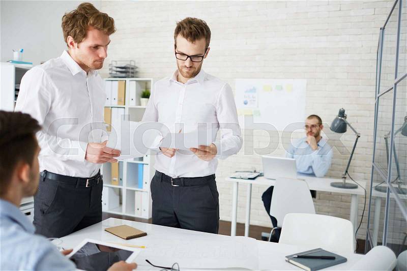 Two engineers with papers brainstorming in office, stock photo