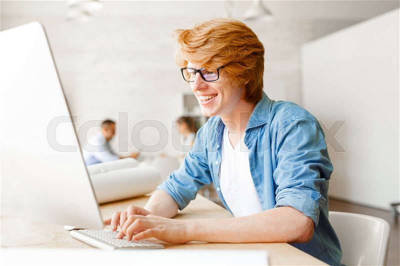 Creative young man typing in front of computer at workplace, stock photo