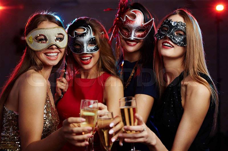 Girls in masks toasting with champagne at party, stock photo