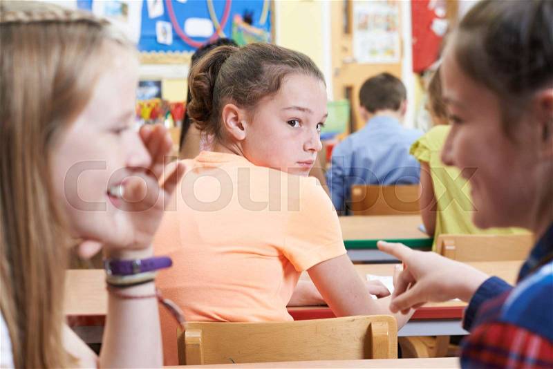 Unhappy Girl Being Gossiped About By School Friends In Classroom, stock photo