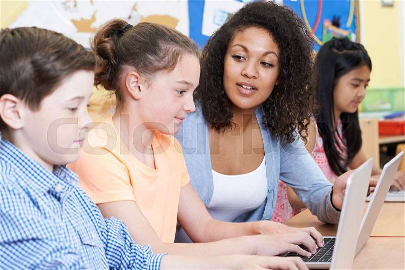 Teacher Helping Female Elementary Pupil In Computer Class, stock photo