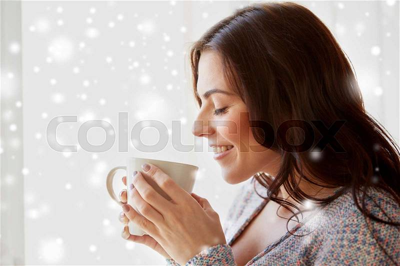 People, drinks, winter, christmas and bliss concept - happy young woman with cup of tea or coffee at home over snow, stock photo