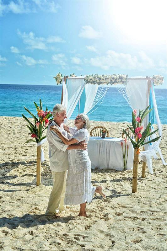 Happy elderly couple dancing at tropical beach, stock photo