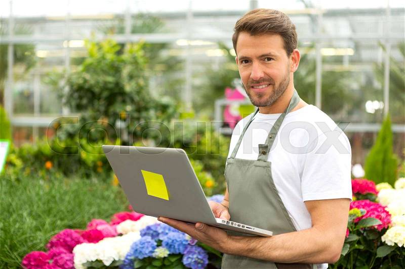 View of a Young attractive man working at the plants nursery using laptop, stock photo