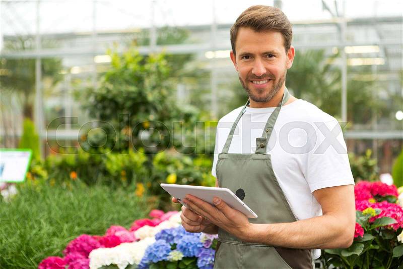 View of a Young attractive man working at the plants nursery using tablet, stock photo