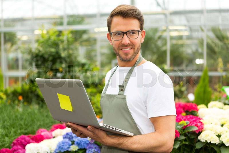 View of a Young attractive man working at the plants nursery using laptop, stock photo