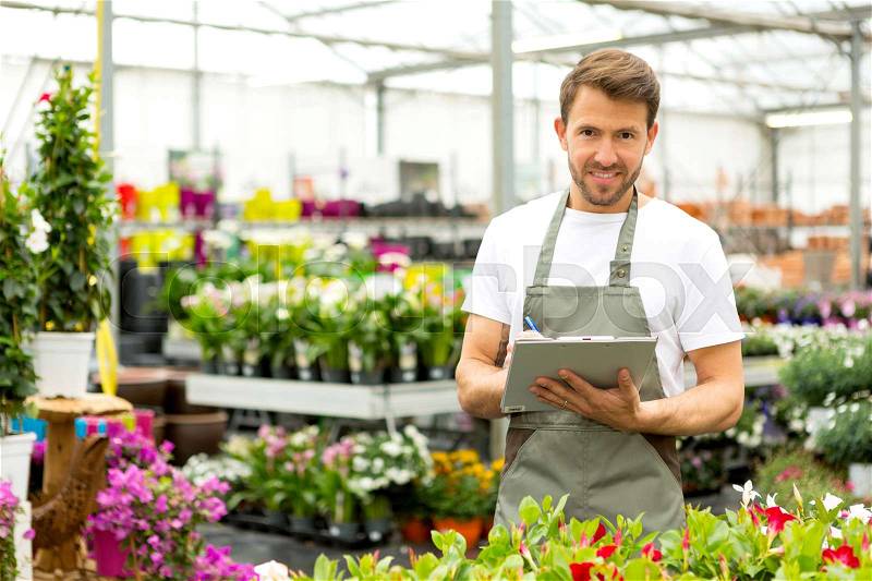 View of a Young attractive man writing notes at the plants nursery , stock photo