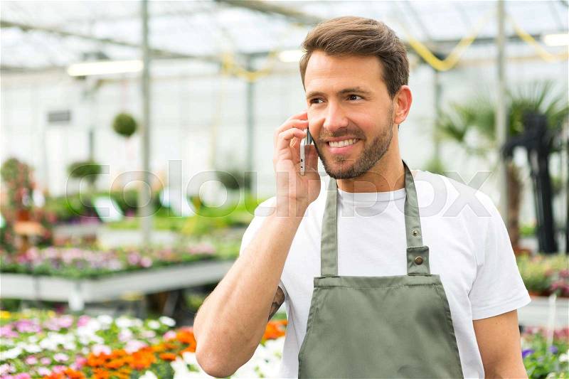 VIew of a Young attractive man working at the plants nursery using smartphone, stock photo