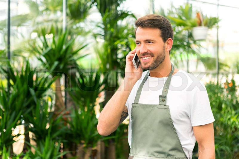 VIew of a Young attractive man working at the plants nursery using smartphone, stock photo