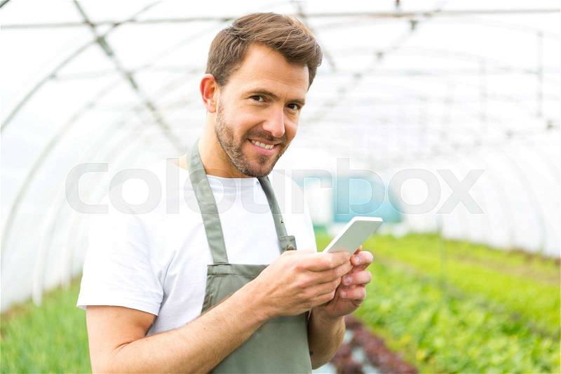 Portrait of an attractive farmer in a greenhouse using mobile, stock photo