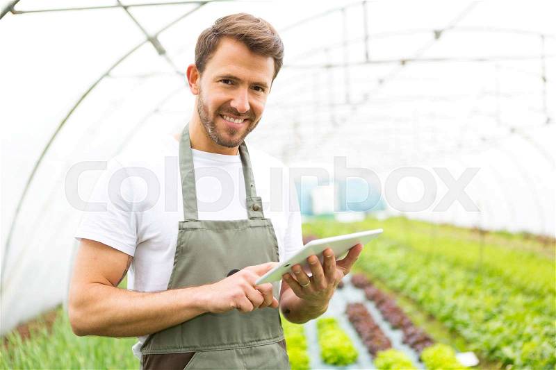 Portrait of an attractive farmer in a greenhouse using tablet, stock photo