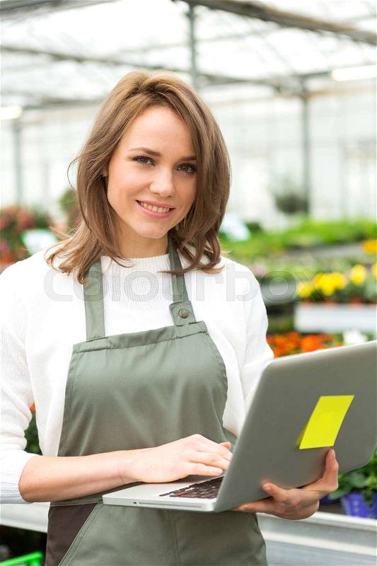 View of a Young attractive woman working at the plants nursery using laptop, stock photo