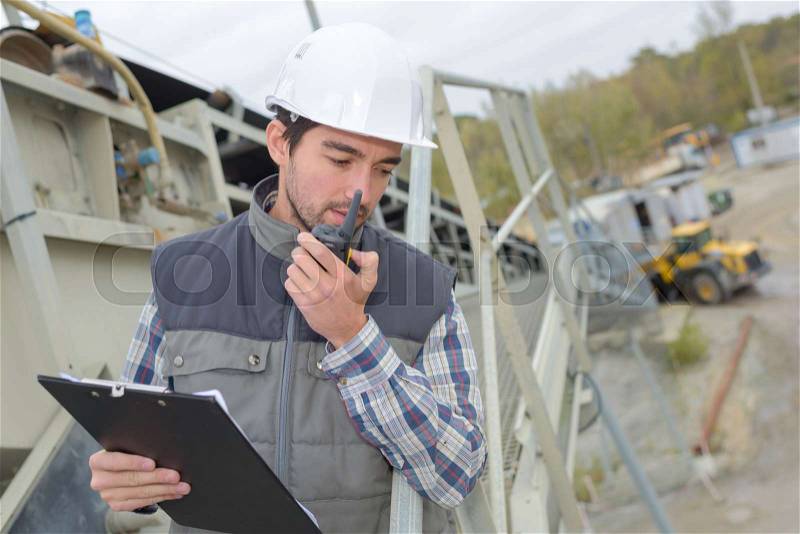 Man in construction site with clipboard and walkie talkie, stock photo