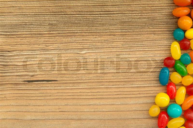 Colorful jelly beans shaped a frame to write your text on a wooden background, stock photo