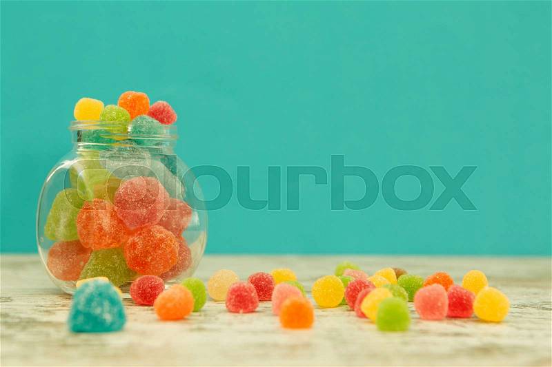 Glass jar full of jelly beans on a wooden table with blue background, stock photo