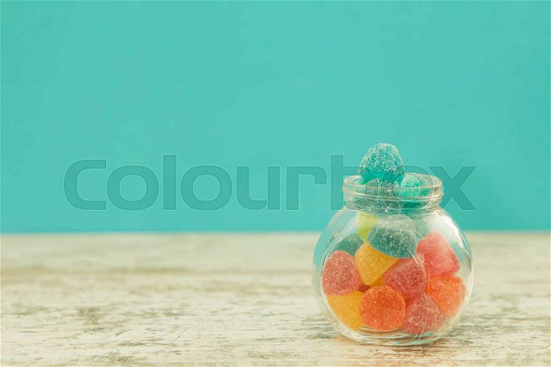 Glass jar full of jelly beans on a wooden table with blue background, stock photo