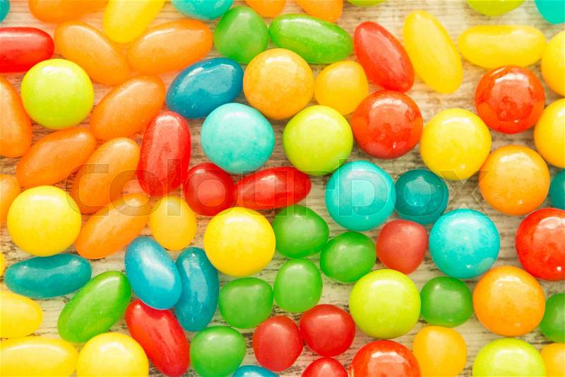 Colorful jelly beans of different sizes close to wallpaper, stock photo