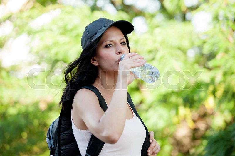 Beautiful woman drinking water while hiking through the countryside, stock photo