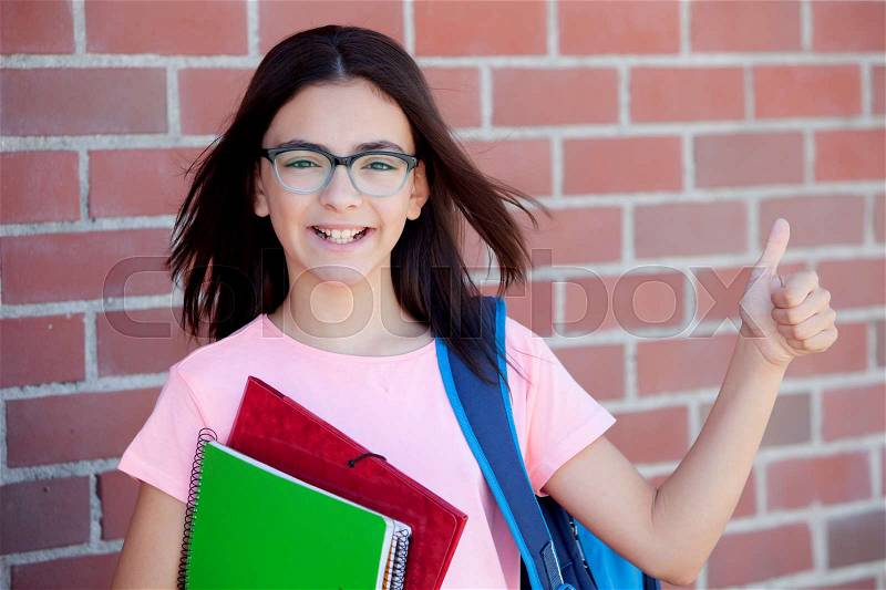 Preteenager girl next to a red brick wall with the backpack and books saying Ok, stock photo