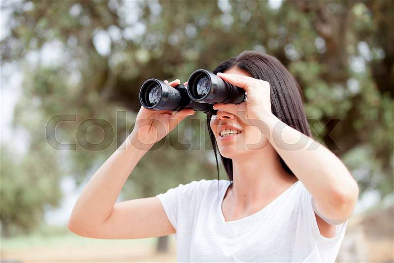 Brunette woman in the park looking through binoculars, stock photo