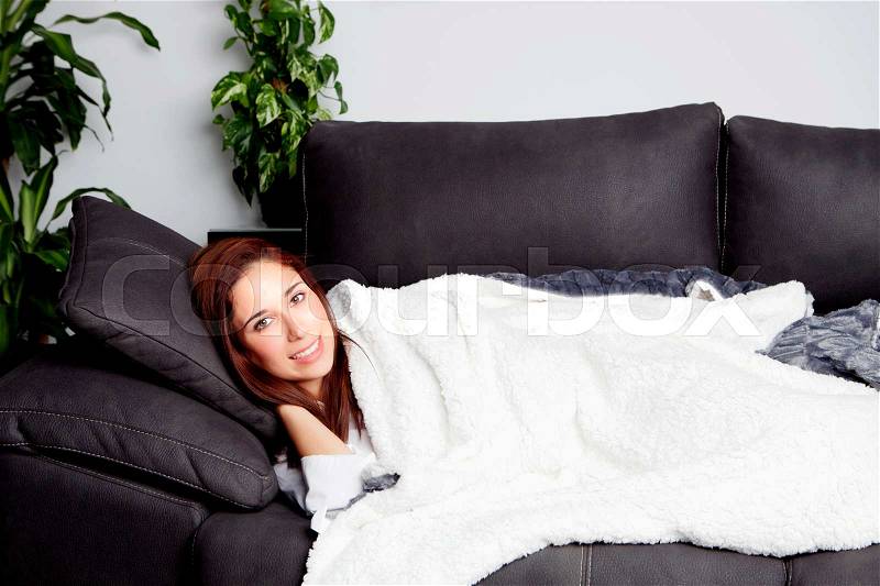 Attractive girl lying on the couch covered with a blanket, stock photo