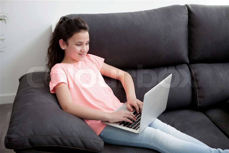Little girl with a laptop in the sofa at home, stock photo