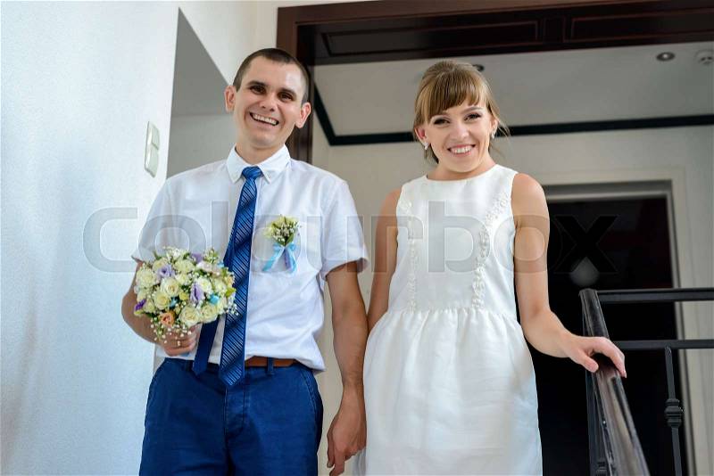 Happy young newlyweds leaving the bridal office pausing on the steps holding hands to smile at the camera, stock photo