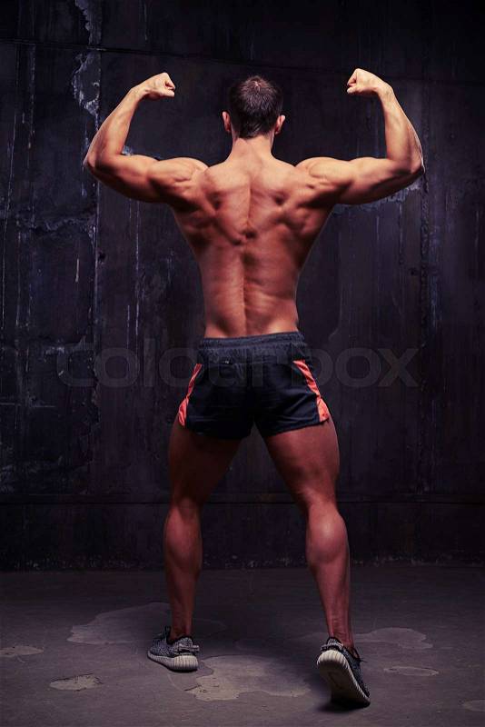 Male fitness model is standing with his back to the camera in bodybuilder pose emphasizing every muscle on his reliefed trained back, stock photo