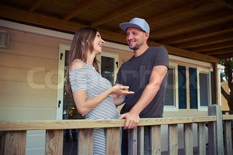 Mid shot of pleasantly talking married couple. They are talking with each other while standing on the porch of the wooden rest house. Smiling, looking happy and excited , stock photo
