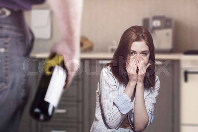 Woman victim of domestic violence and abuse. Woman scared of a man holding a bottle, stock photo