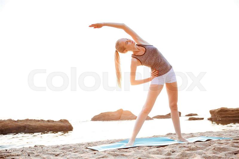 Beautiful young woman stretching hands during yoga on the beach, stock photo