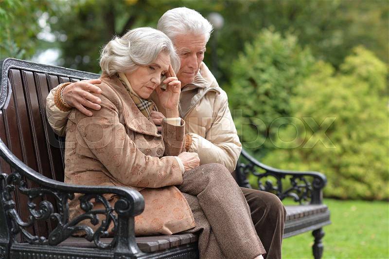 Portrait of a sad elderly couple sitting on a bench in autumn park, stock photo
