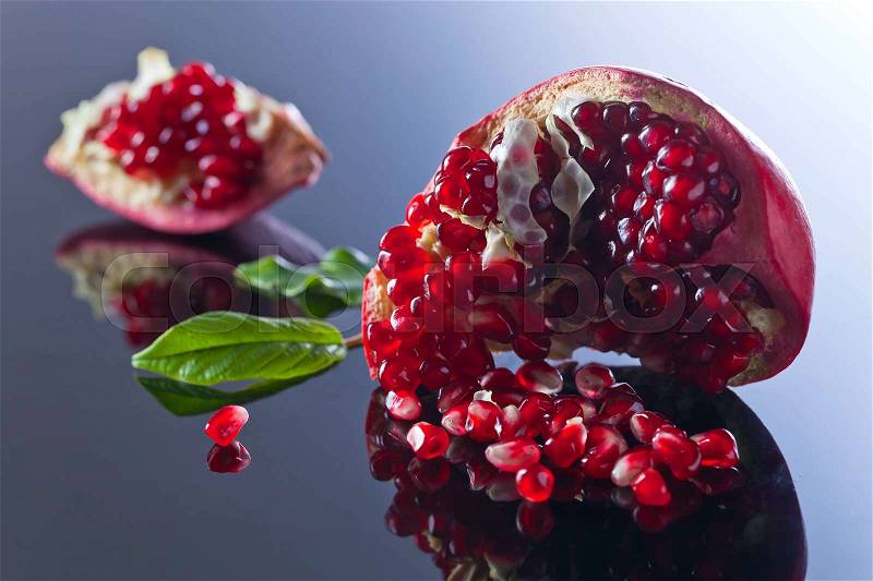 Broken ripe pomegranate with leaves on a reflective background, stock photo