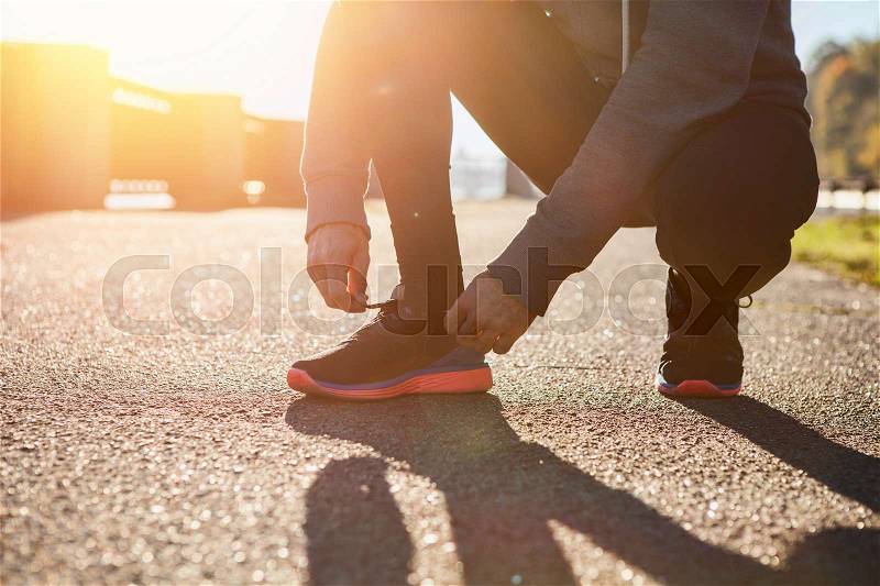Man tying jogging shoes on sunset, stock photo